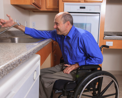 Man with quadriplegia using a manual wheelchair reaches for the sink tap over a kitchen counter.