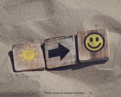 Tiles in the sand of a sun pointing toward happiness.