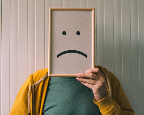 Man holding bulletin board in front of his face with an unhappy face drawn on the board