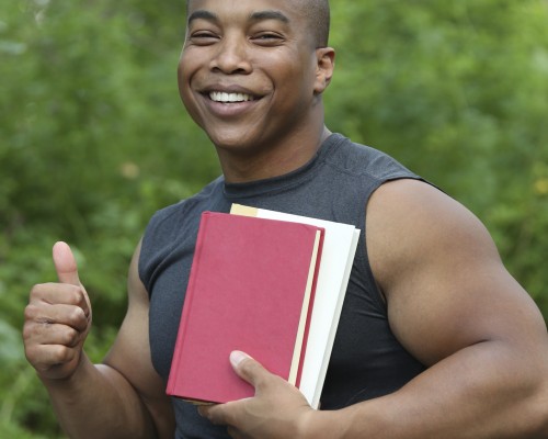 a smiling muscular student sitting in his wheelchair hold books in one hand and thumb up with the other