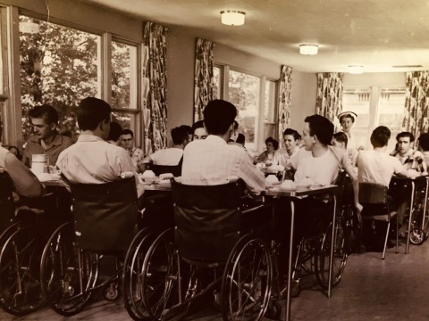 Many men sitting at tables in Lyndhurst Lodge ready for a meal.